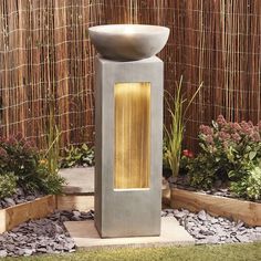 an outdoor water fountain in the middle of a garden with plants and rocks around it