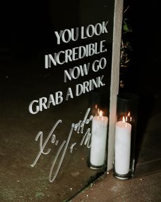 two candles are lit in front of a sign that reads, you look incredible now go grab a drink