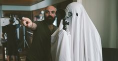 a man pointing at the camera in front of a white curtain and some other items