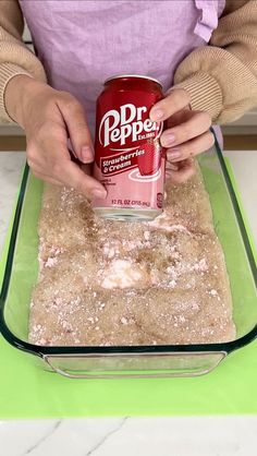 a person in an apron holding a can of dr pepper on top of some food