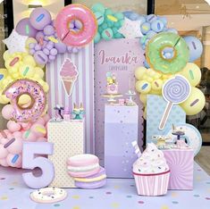 a table topped with lots of balloons and donuts next to a sign that says happy 5th birthday