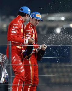 two men standing next to each other on top of a race track in the rain