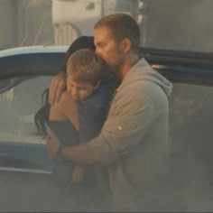 a man holding a boy in his arms while standing next to a car on the street