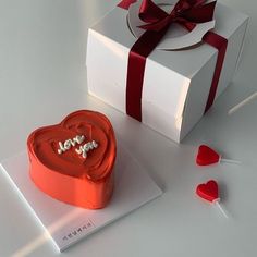 a heart shaped cake sitting on top of a table next to a white box with a red ribbon