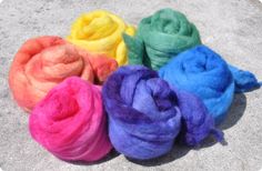 four skeins of dyed wool in different colors on the cement floor with one spinning