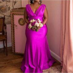 a woman in a long purple dress holding a flower bouquet standing next to a pink wall