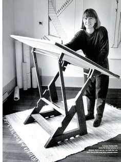 a woman standing next to a wooden table on top of a white rug in front of a stair case