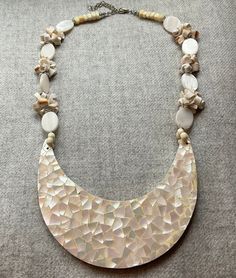 "This stunning mother of pearl crescent inlay focal necklace features a genuine shell clusters and oval mother of pearls. There is a 2\" extension chain, and fastens with a secure lobster clasp. The mosaic inlay crescent has an aurora borealis effect, with subtle pinks, greens and lavenders. Condition:  Very Good Vintage Condition. There is some minor loss to the shell inlay on the very edge at left hand side of the crescent.   Measurements: Crescent 4-3/4\" X 1-3/4\" 21\" Circumference  Include Mother Of Pearl Mosaic, Shell Island, Mosaic Inlay, Shell Mosaic, Fancy Jewelry Necklace, Book Necklace, Mother Of Pearl Jewelry, Bib Necklaces, Fancy Jewelry