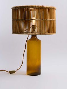 a brown glass bottle with a wicker lamp shade on the bottom and a cord attached to it