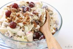 a salad with grapes, nuts and cheese in a glass bowl next to a wooden spoon