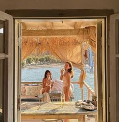 two women sitting at a table with drinks in front of them, looking out onto the water