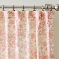 a pink and white floral curtain hanging on a metal rod in front of a window