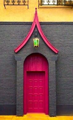 a red door is in front of a gray building with a pink roof and window