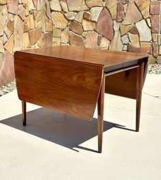 a wooden desk sitting on top of a sidewalk next to a wall covered in rocks