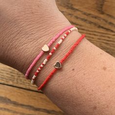 two bracelets with heart charms on the wrist, one pink and one red string