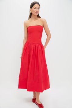 a woman is wearing a red dress with a strapless neckline and pleaed skirt