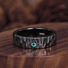 a black ring with a green stone in the center on top of a wooden table