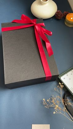 a black box with a red ribbon on top of a table next to a candle