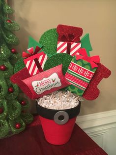 a red bucket filled with lots of candy and gift boxes next to a christmas tree