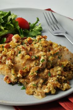 a white plate topped with meat covered in gravy next to a green salad