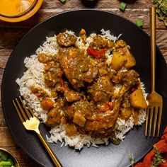 a black plate topped with rice and meat covered in gravy on top of a wooden table