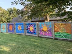 a row of colorful painted wooden fences in front of a house with grass and trees