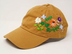 This hand embroidered flower baseball cap is a one-of-a-kind accessory that combines style and comfort. The cap is crafted from high-quality material, ensuring durability and comfort. The intricate floral design is hand-embroidered, giving each cap a unique touch and making it a standout piece. Whether you're running errands or enjoying a day outdoors, this cap will keep the sun out of your eyes in style. Flower is 100% hand embroidered on a 100% cotton wash baseball cap. Hat is one size fits al Brown Embroidered Baseball Cap With Curved Brim, Brown Embroidered Curved Brim Baseball Cap, Yellow Adjustable Dad Hat For Spring, Brown Adjustable Baseball Cap For Spring, Adjustable Brown Baseball Cap For Spring, Yellow Snapback Dad Hat For Spring, Spring Brown Baseball Cap With Curved Brim, Brown Baseball Cap For Spring, Brown Baseball Cap With Visor For Spring