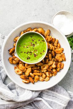 a white bowl filled with green sauce next to some fried food on top of a plate