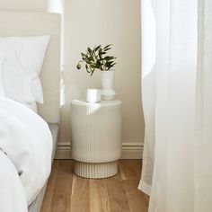 a white bed sitting next to a tall window with curtains on both sides and a plant in the corner