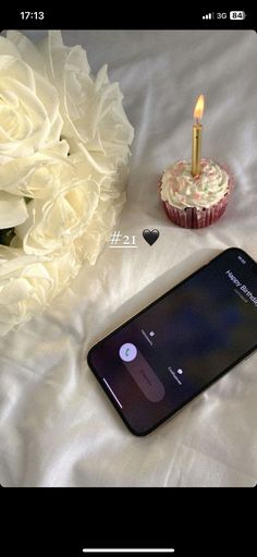 a cell phone sitting on top of a bed next to a cupcake