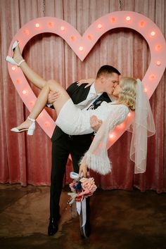 a bride and groom kissing in front of a neon heart