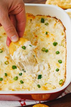 a person dipping cheese into a casserole dish with crackers on the side