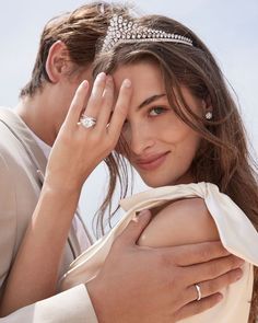 a man and woman are posing for the camera with rings on their fingers, one is wearing a tiara