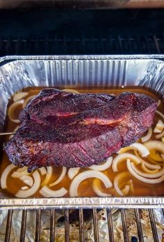 a steak roasting in oil on top of some onions and broth over an open grill