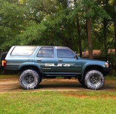 a blue truck parked on top of a dirt road in front of some green trees