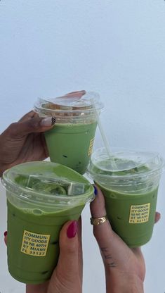 two people holding up green smoothies in plastic cups