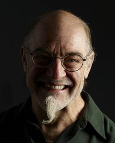 an older man with glasses and a beard smiles for the camera while wearing a green shirt