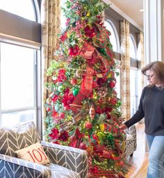 a woman standing next to a christmas tree in a living room with red and green decorations