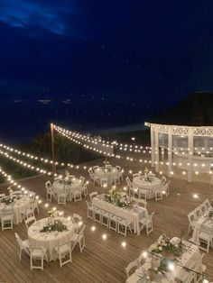 tables and chairs are set up on a deck with string lights