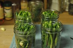 four mason jars filled with green vegetables on top of a table