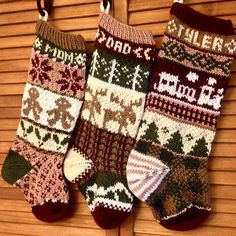 three knitted christmas stockings hanging from hooks on a wooden slatted wall,