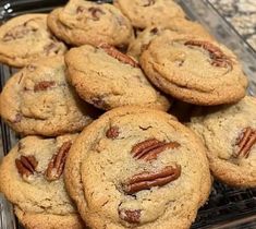 a pile of cookies with pecans on top sitting on a cooling rack in the kitchen