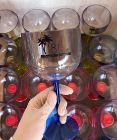 a hand holding a wine glass in front of many glasses with palm trees on them