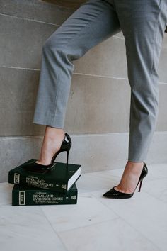 a woman standing on top of a stack of books wearing high heeled black shoes