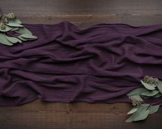 purple fabric with green leaves on it laying on a wooden floor next to a plant