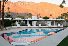 an empty swimming pool surrounded by palm trees and mountains in the background with white lounge chairs around it