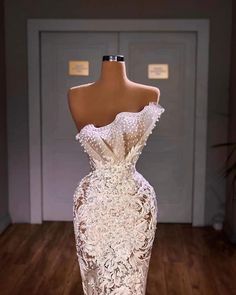 a white dress on display in front of a door with wooden floors and doors behind it