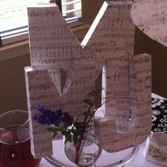 the letters are made out of sheet music and sit on a table next to a vase with flowers