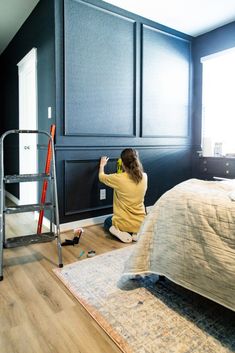 a woman kneeling on the floor next to a ladder in a room with black walls