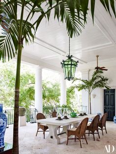 an outdoor dining area with wicker chairs and white table surrounded by palm trees in the background